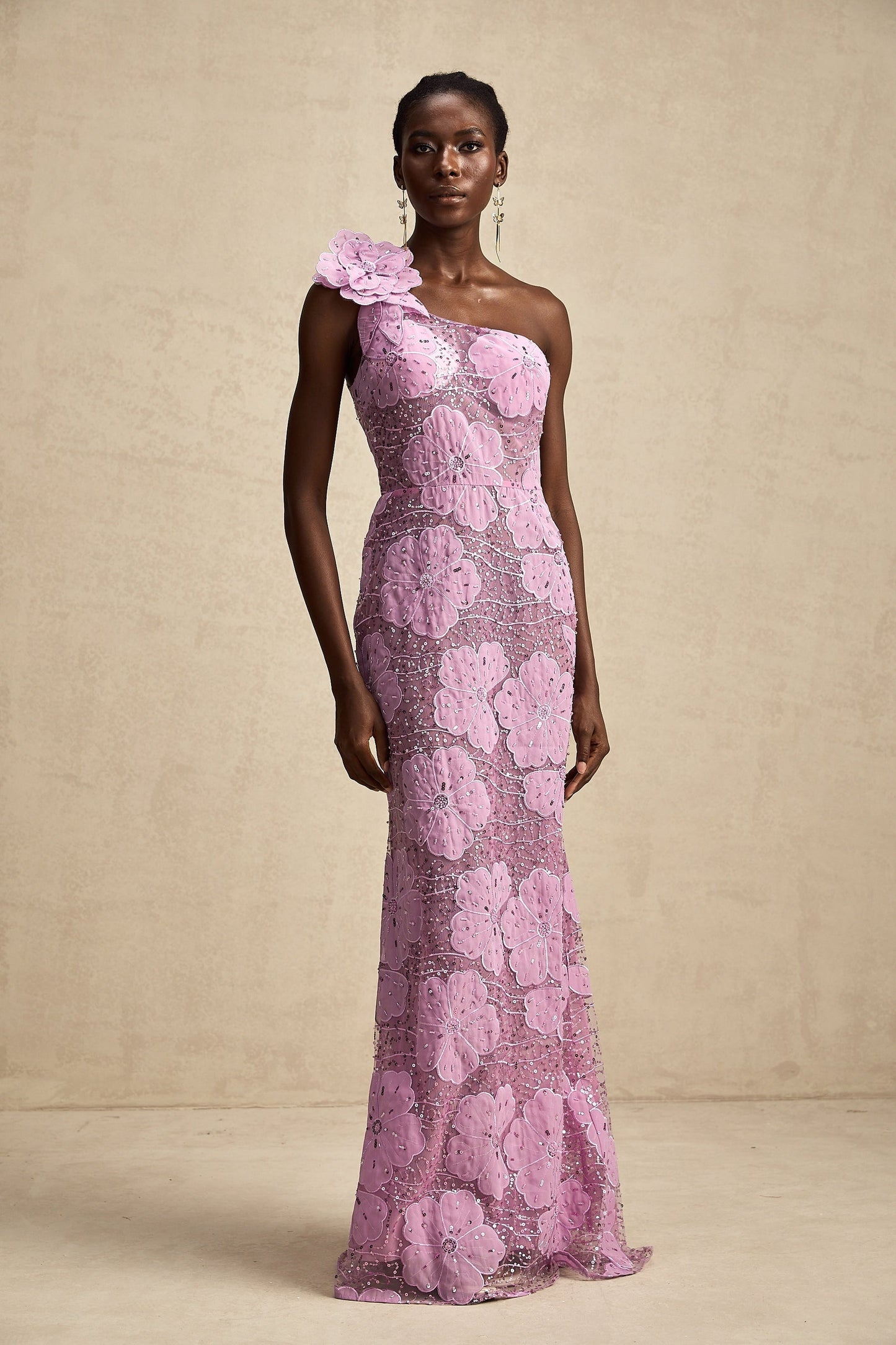 A long purple maxi dress with floral appliqué details worn by a model standing in a neutral setting