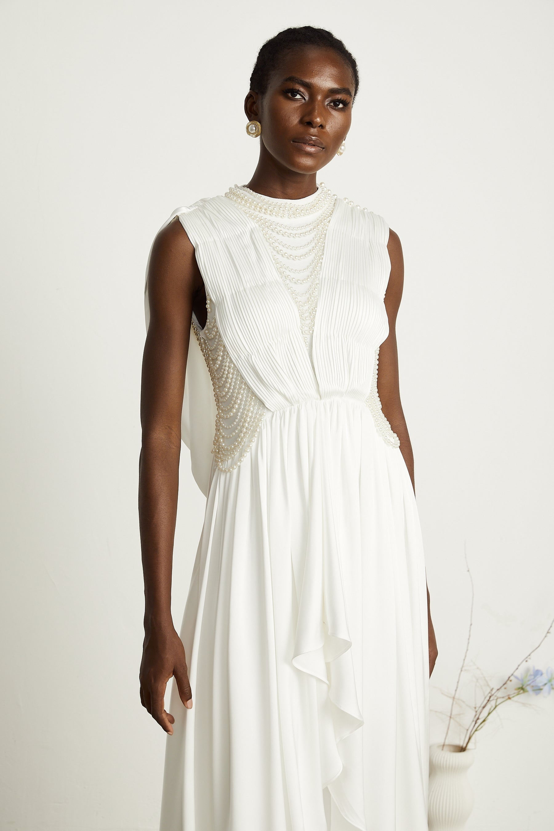 A long white pleated maxi dress adorned with faux pearl accents on a mannequin or model showcasing the elegant flowing design