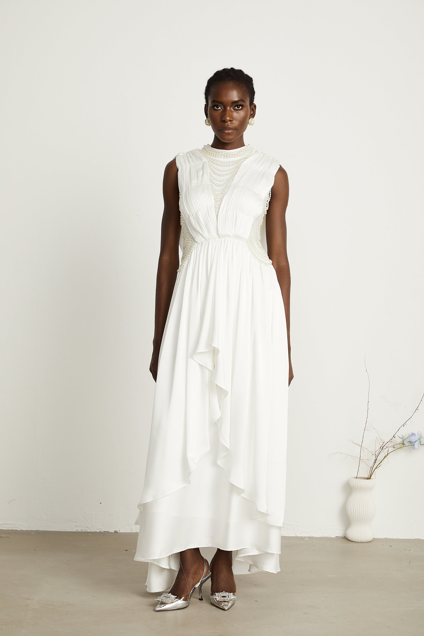 A long white pleated maxi dress with faux pearl embellishments on a female model