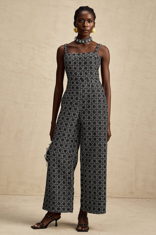 a black tweed jumpsuit with a diamond pattern standing in a neutral setting