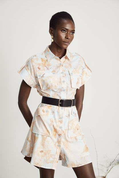 A woman wearing a short white shirt dress with a belt cinched at the waist the dress has a collar and buttons down the front