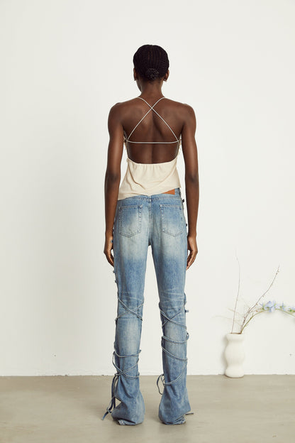 A woman wearing blue denim jeans with decorative straps on the sides standing in a casual pose