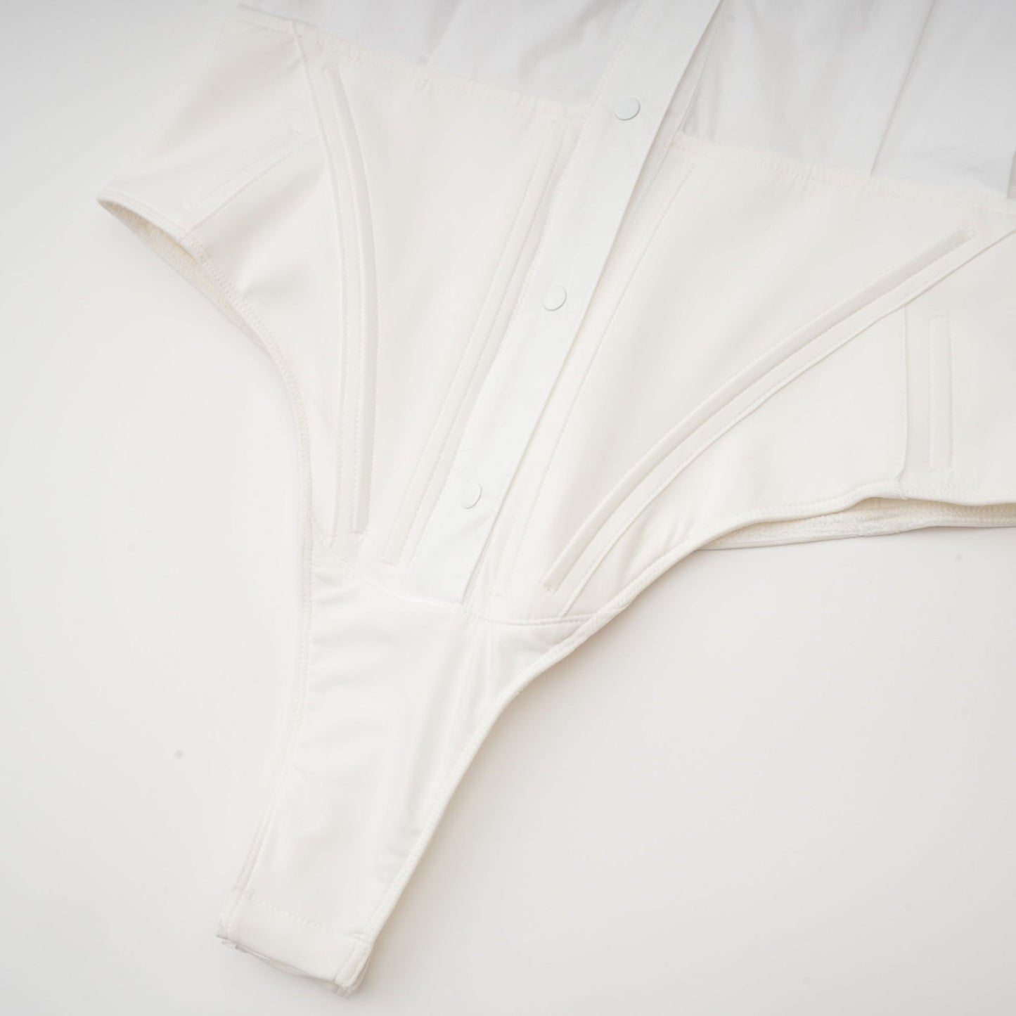 white cottonpoplin bodysuit with jersey trim and thong style bottom featuring thin straps and a snap closure