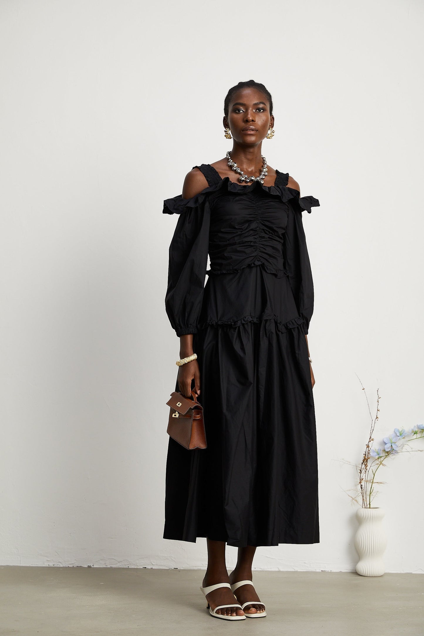 A black pleated midi dress with ruffled details and a flowy silhouette