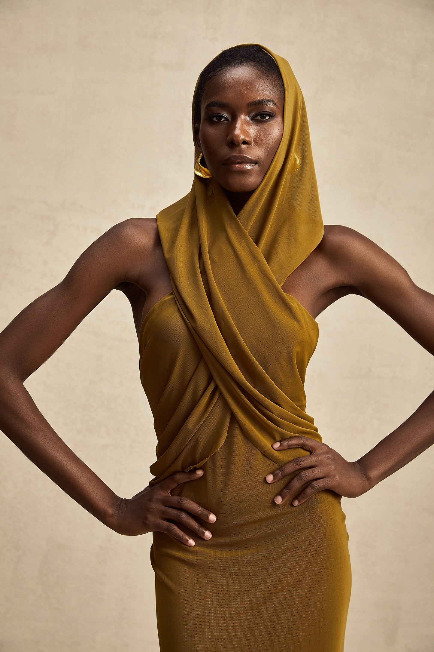 Woman wearing a long flowing maxi dress with a crossover front hood and open back design in a solid color