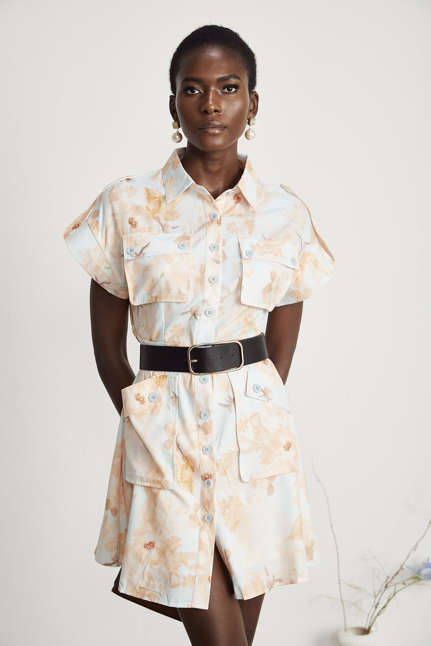 Woman wearing a short white shirt dress with a belt at the waist and buttonup front