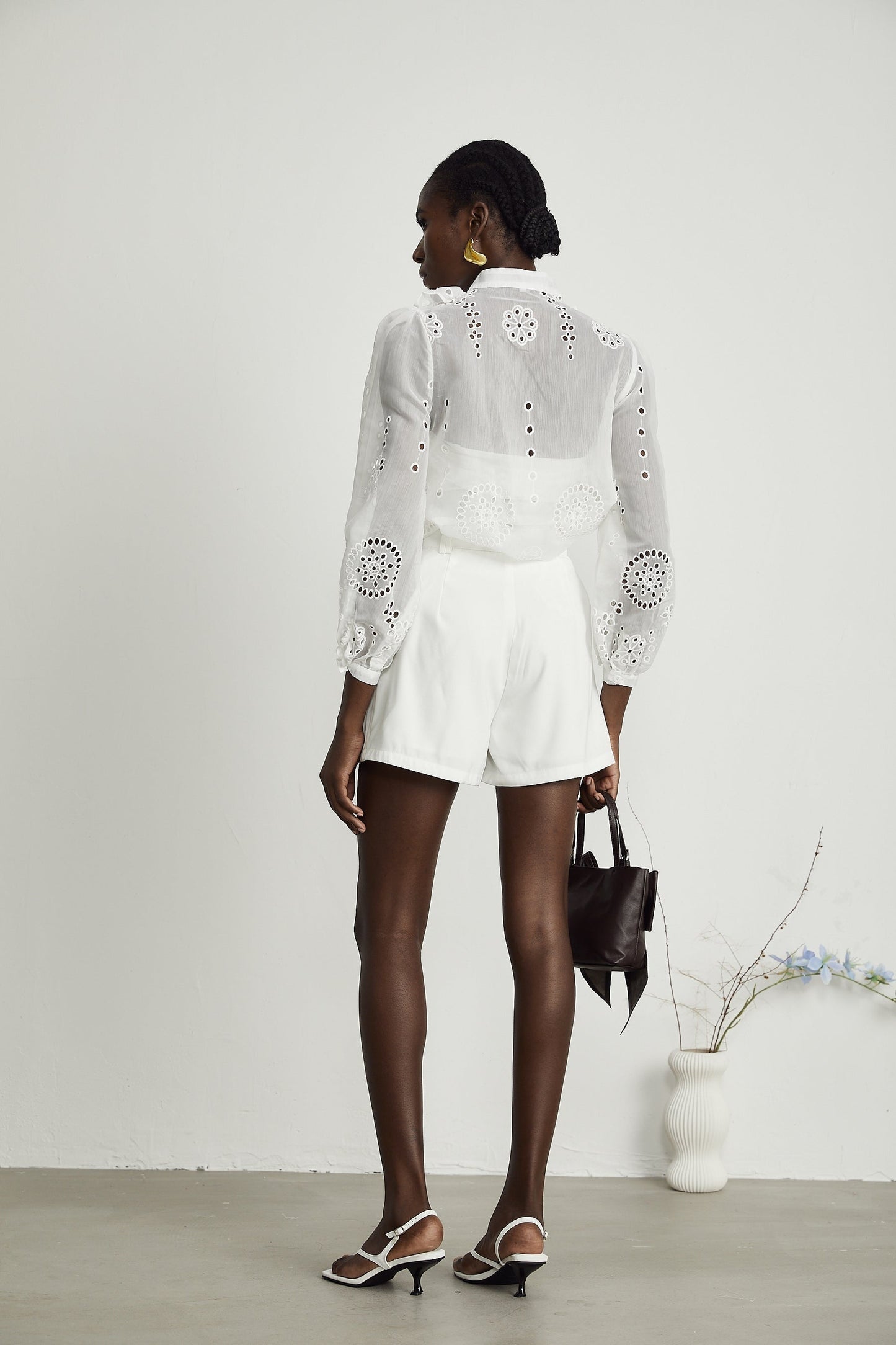 Woman wearing white ruffled shirt with cutout details and matching shorts set against plain background