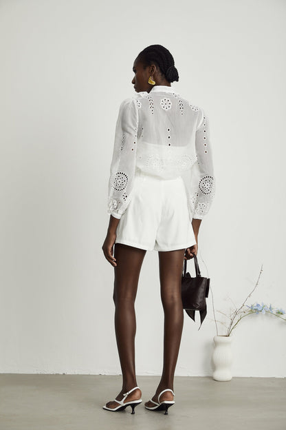 Woman wearing white ruffled shirt with cutout details and matching shorts set against plain background