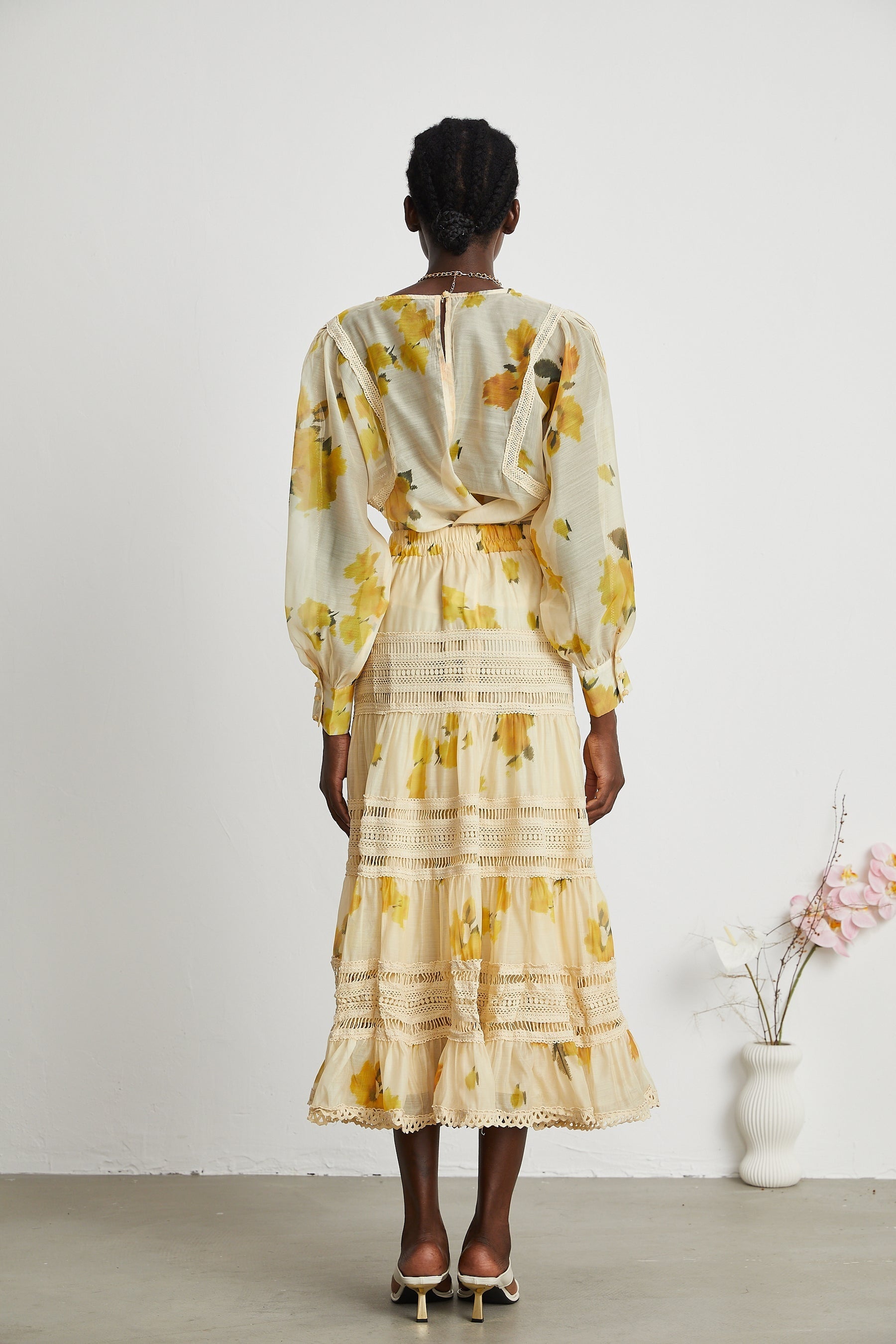 Back view of woman wearing yellow floral print dress with lace trim